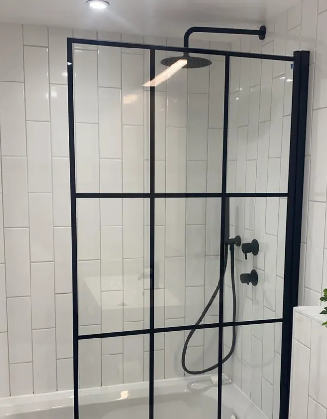 Matt black framed shower screen over a bath with vertical white tiles